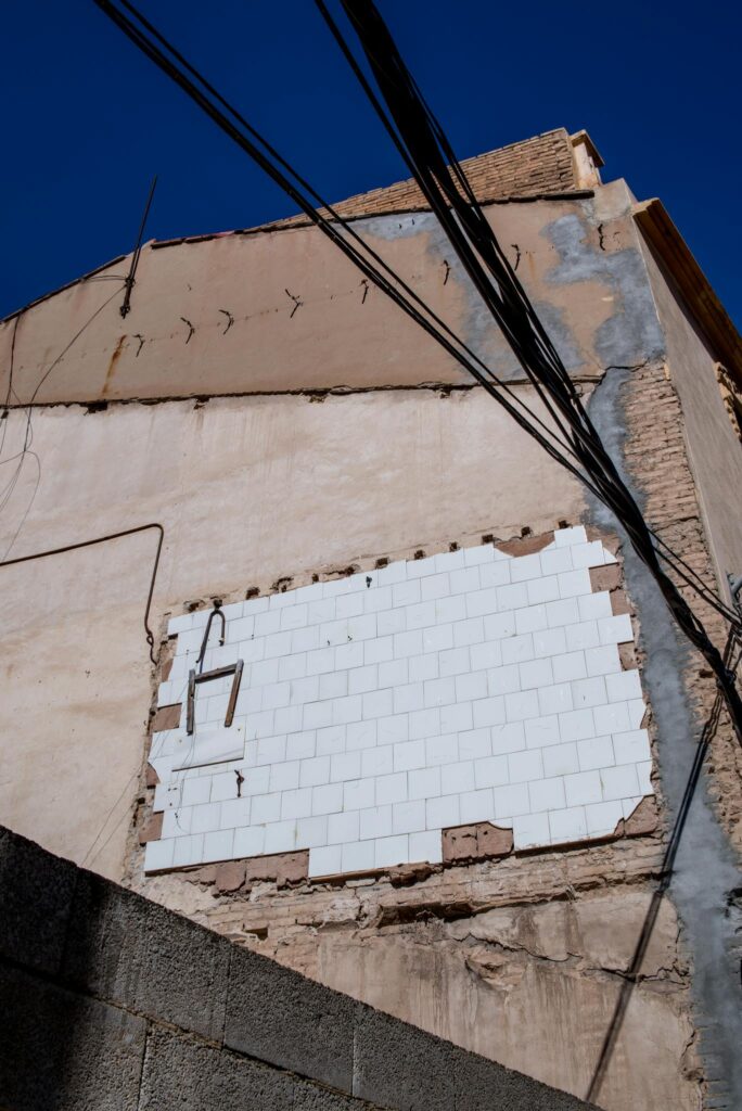 Crumbling building facade showcasing urban decay and overhead wires under clear blue sky.