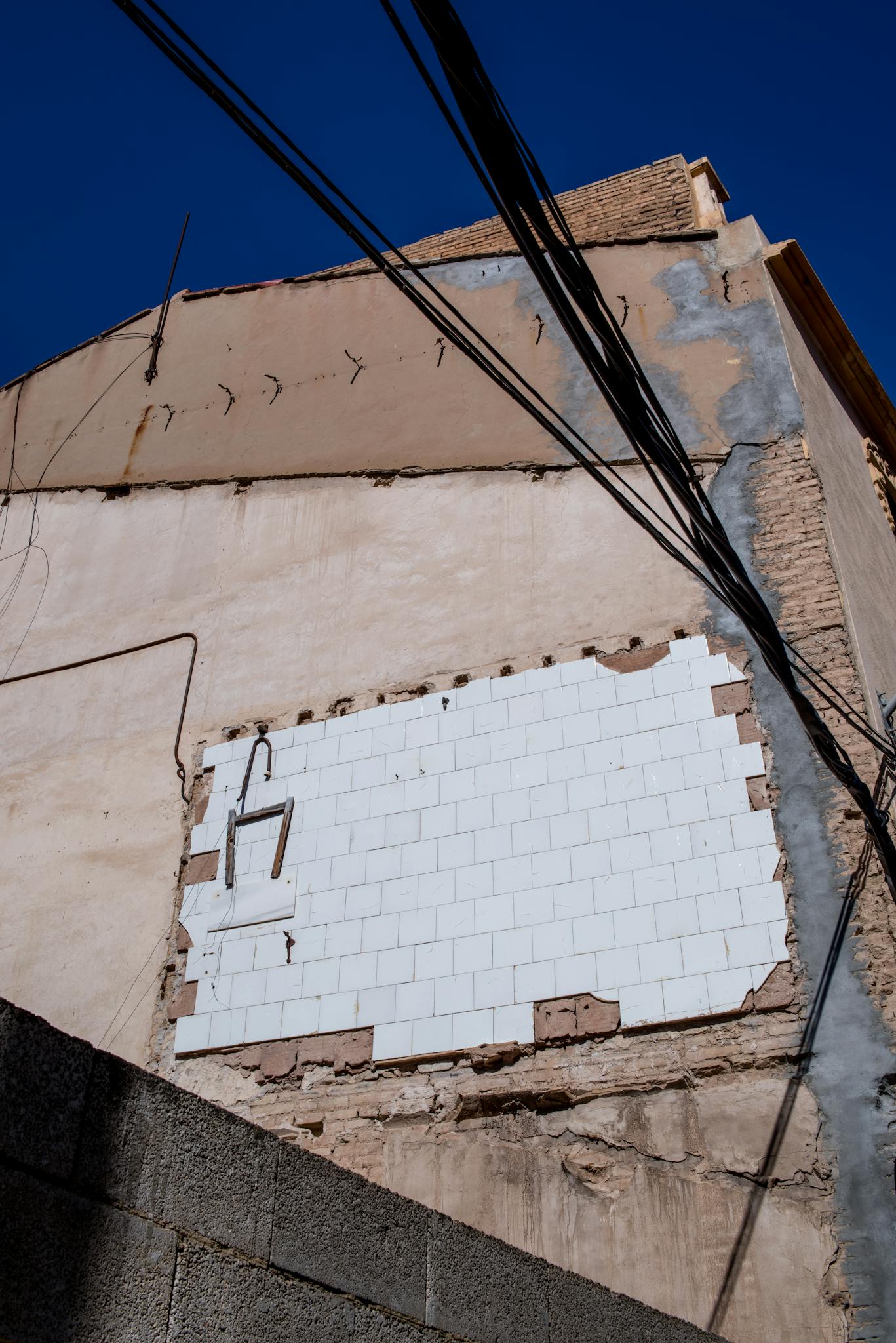 Crumbling building facade showcasing urban decay and overhead wires under clear blue sky.