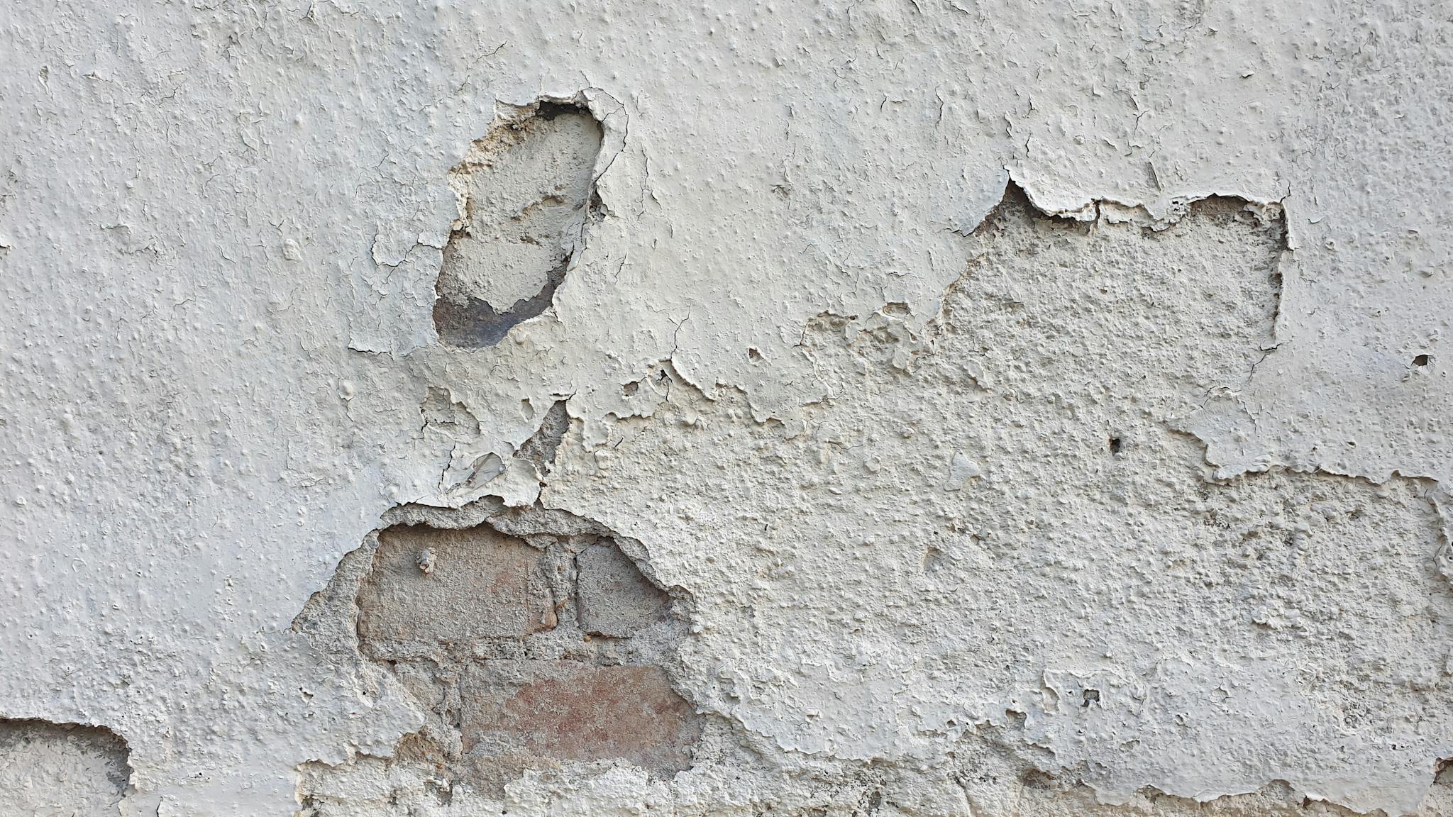 Detailed view of a worn and cracked wall surface with peeling paint and exposed bricks.