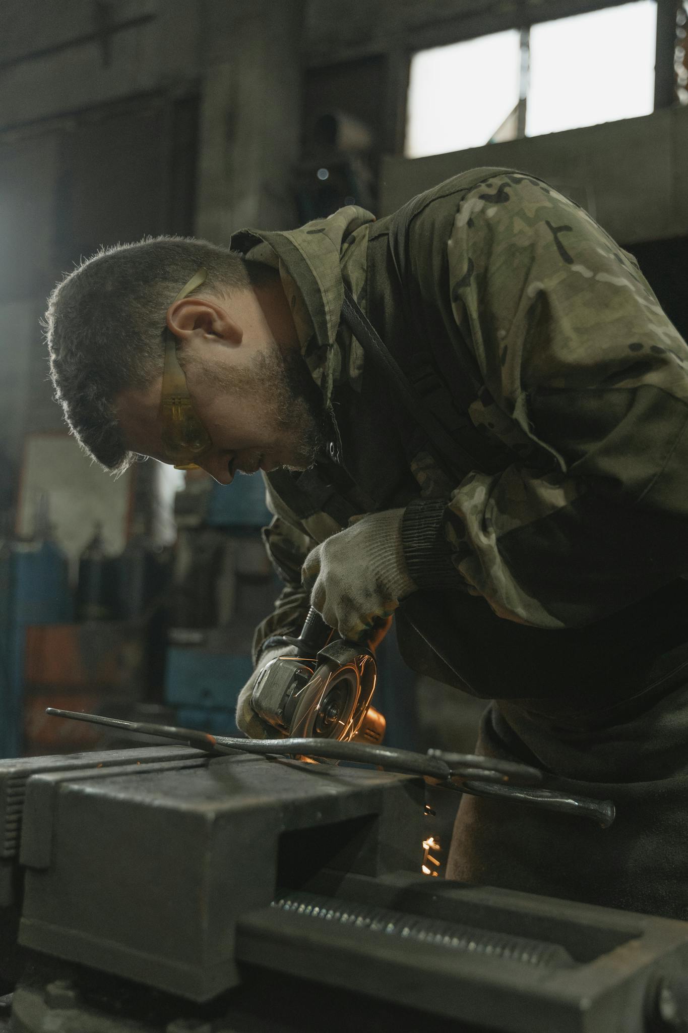 Focused craftsman at work using a power tool in a dimly lit workshop, showcasing skillful metalwork.